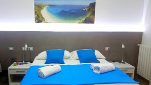 Une chambre d’hôtel avec un lit, deux tables de chevet, un tableau représentant une plage et une couvre-lit bleue.