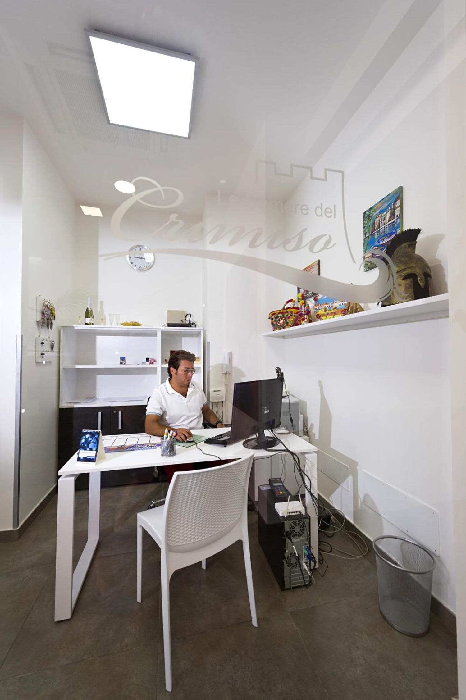 Un bureau moderne avec un bureau, un ordinateur et une chaise. On y trouve une étagère avec des objets décoratifs et une horloge au mur.