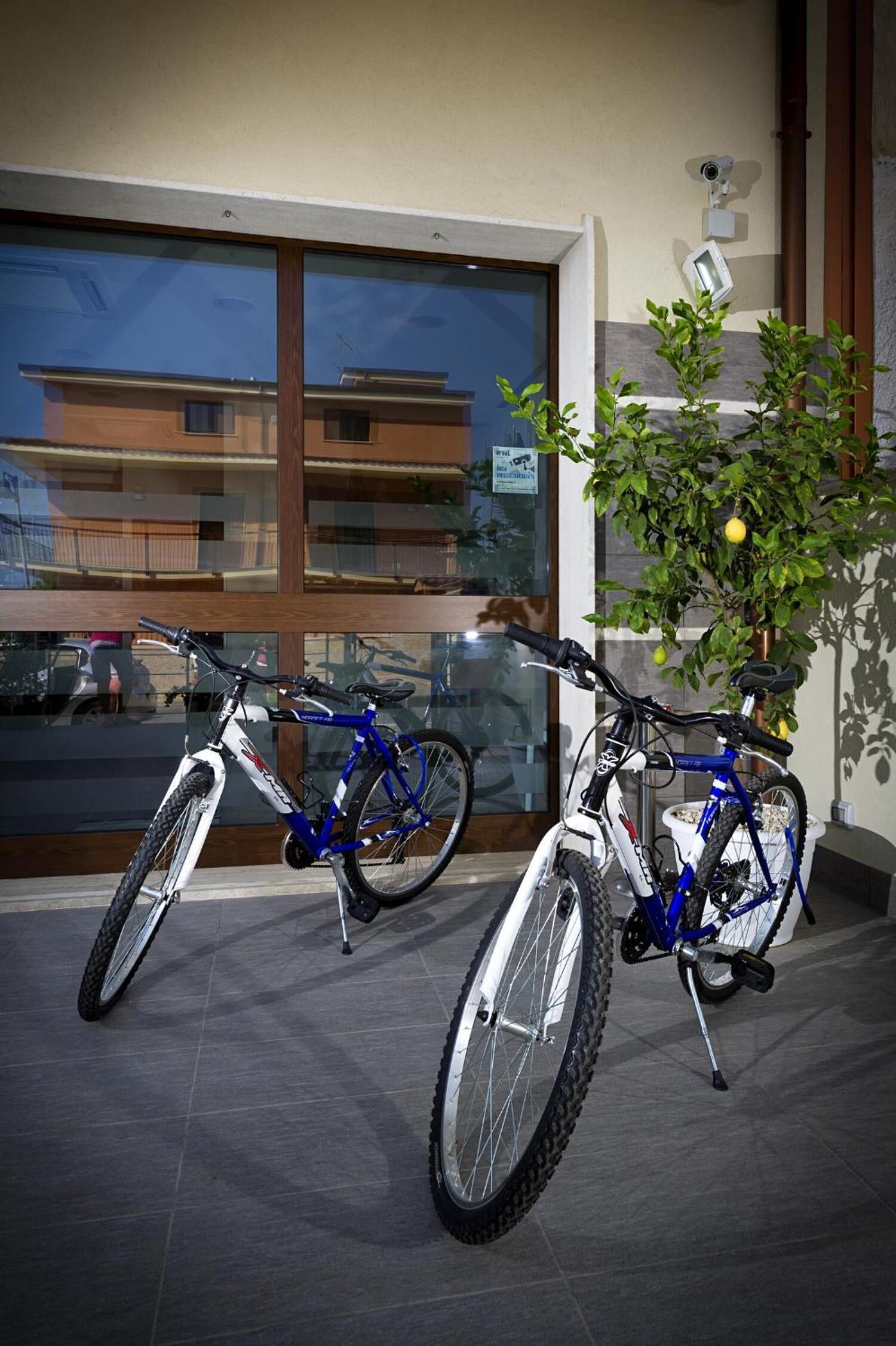 Two bicycles parked indoors near a window with a view of a building outside.