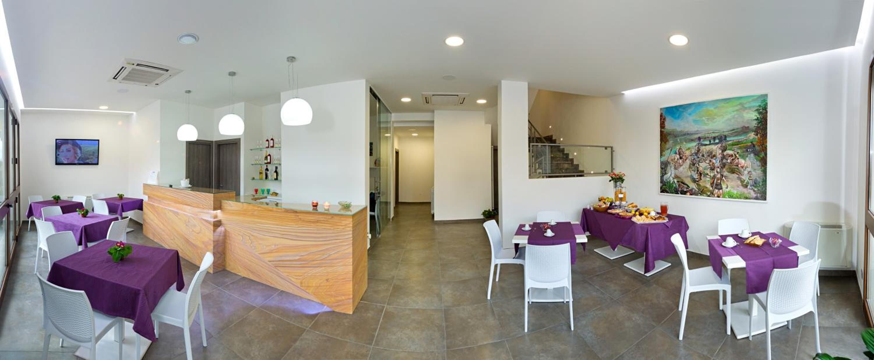 Un restaurante con manteles morados, sillas blancas y un mostrador de recepción de madera.