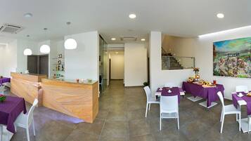 A restaurant with purple tablecloths, white chairs, and a wooden reception desk.