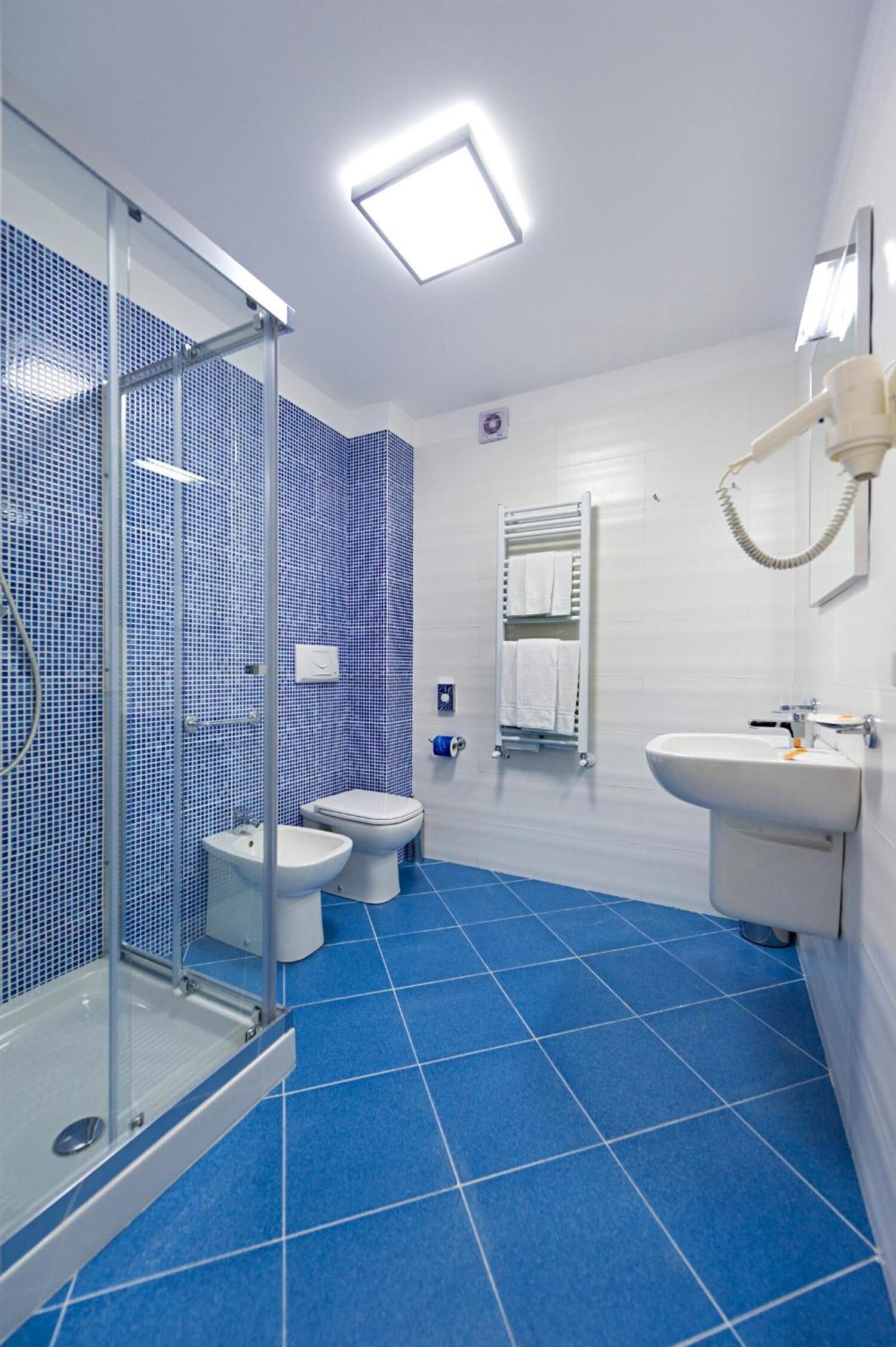 Un baño moderno con cabina de ducha de vidrio, dos inodoros, un lavamanos y un espejo.