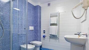 Un baño moderno con cabina de ducha de vidrio, dos inodoros, un lavamanos y un espejo.