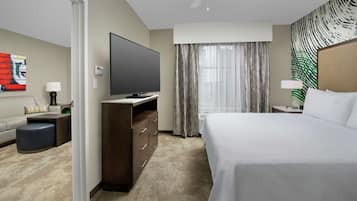 A hotel room with a bed, a flat-screen TV, a desk with drawers, a sofa, and a coffee table.