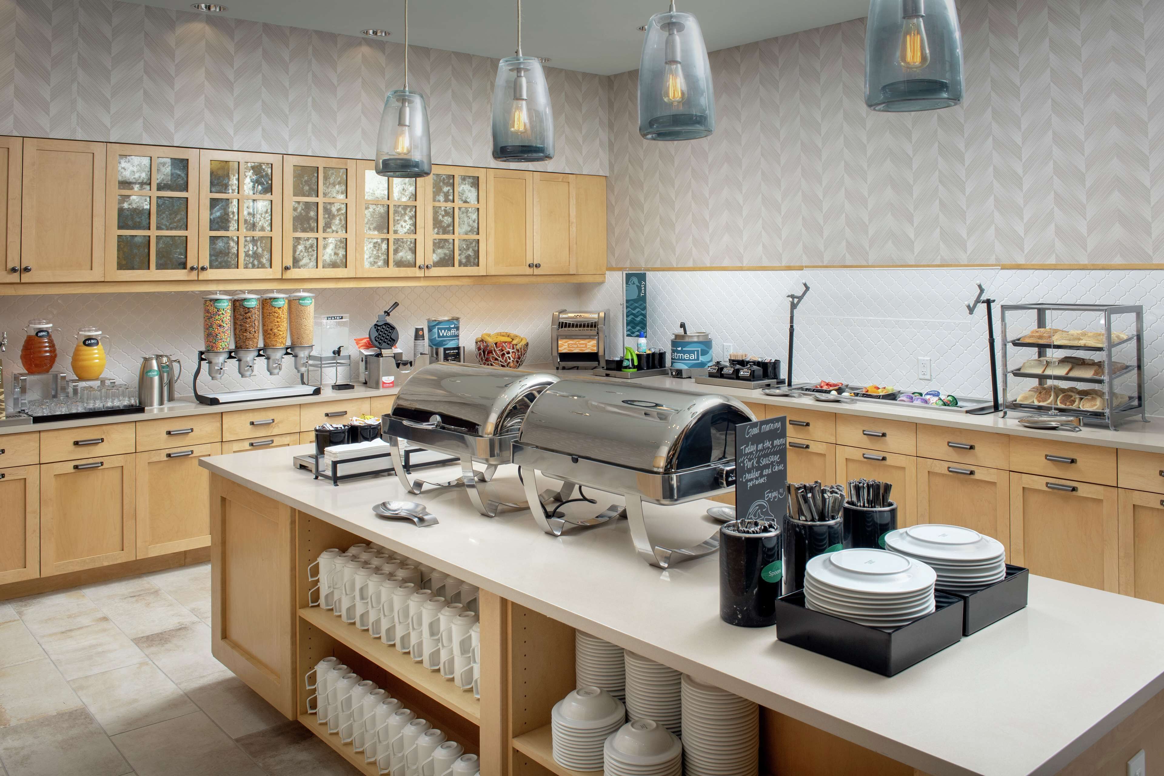 A modern kitchen with a buffet setup, including a coffee machine, waffle maker, and various food dispensers.