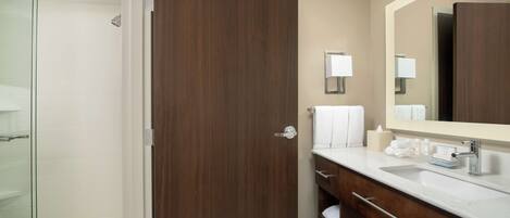 A modern bathroom with a glass shower, a wooden door, a large mirror, and a white sink with a vanity.