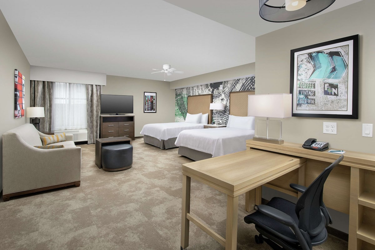 Ett hotellrum med två sängar, ett skrivbord, en stol, en TV och en takfläkt.