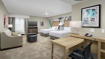 A hotel room with two beds, a desk, a chair, a TV, and a ceiling fan.