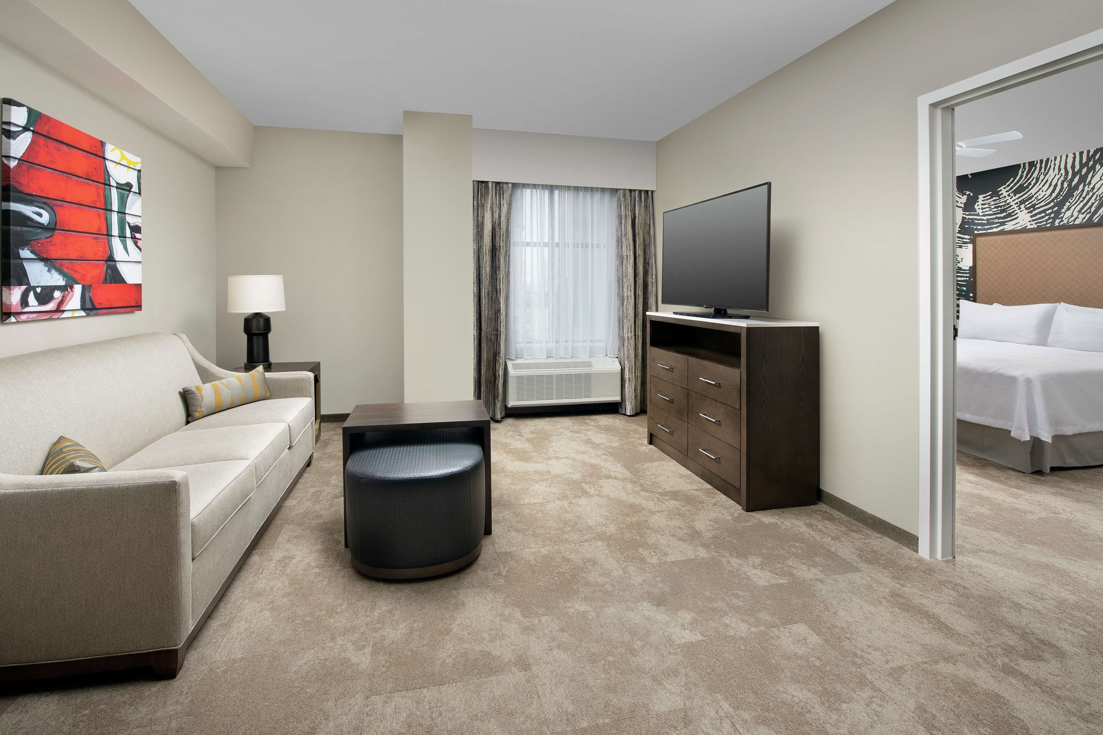 A hotel room with a sofa, a small table, a television, a cabinet, and a bed.