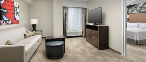 Une chambre d’hôtel avec un canapé, une petite table, un téléviseur, une armoire et un lit.