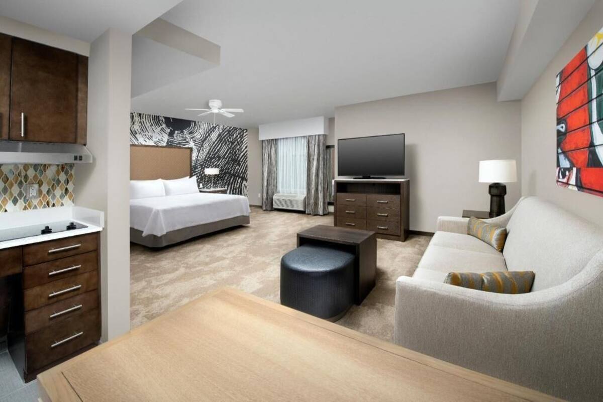 Ett hotellrum med en säng, en tv, en soffa, ett skrivbord och ett matbord.