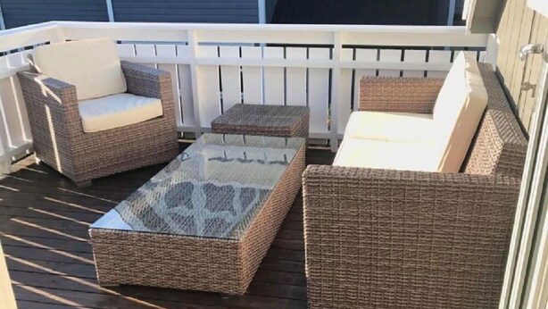 Eine überdachte Terrasse mit Korbmöbeln und einem Tisch mit Glasplatte.