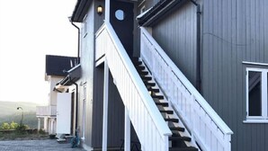 Ein modernes Gebäude mit grauem Außenbereich, einer weißen Treppe, die zu einem überdachten Eingang führt, und einem gepflasterten Weg.