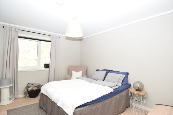 A bedroom with a bed, a bedside table, a lamp, and a window with curtains. - Solferie Holiday Home Bordalssvingen (Kristiansand)