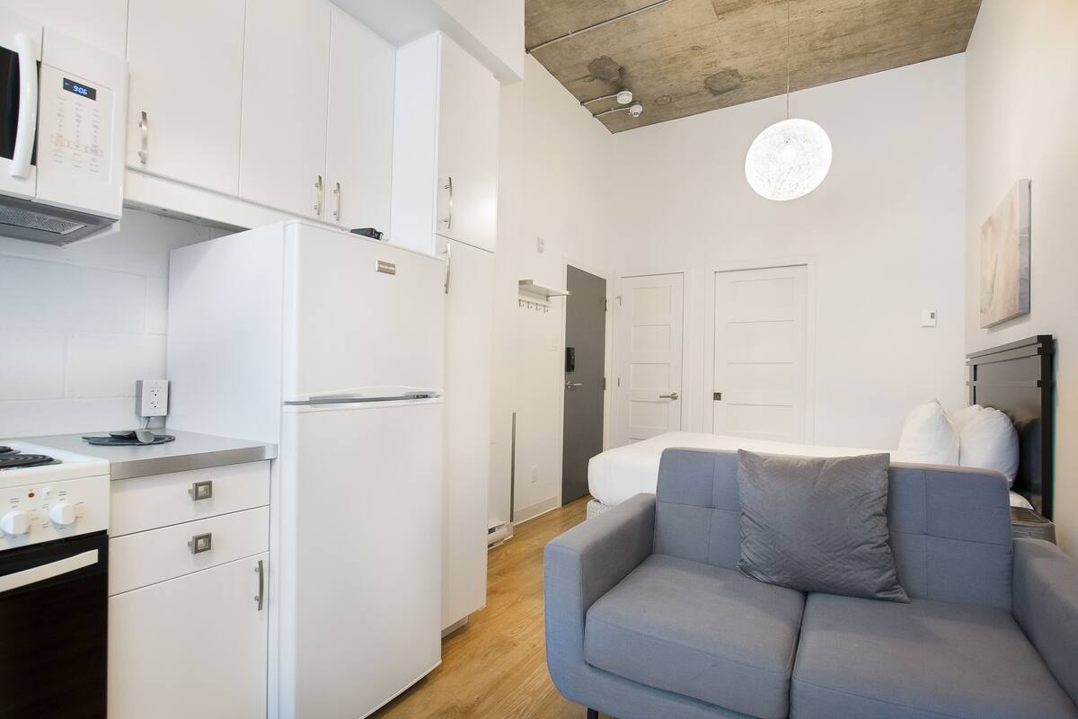 A compact kitchen with white appliances, a grey sofa, and a ceiling with exposed beams.