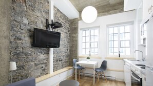 Una cocina moderna con pared de piedra, televisor de pantalla plana, comedor con sillas y horno empotrado.