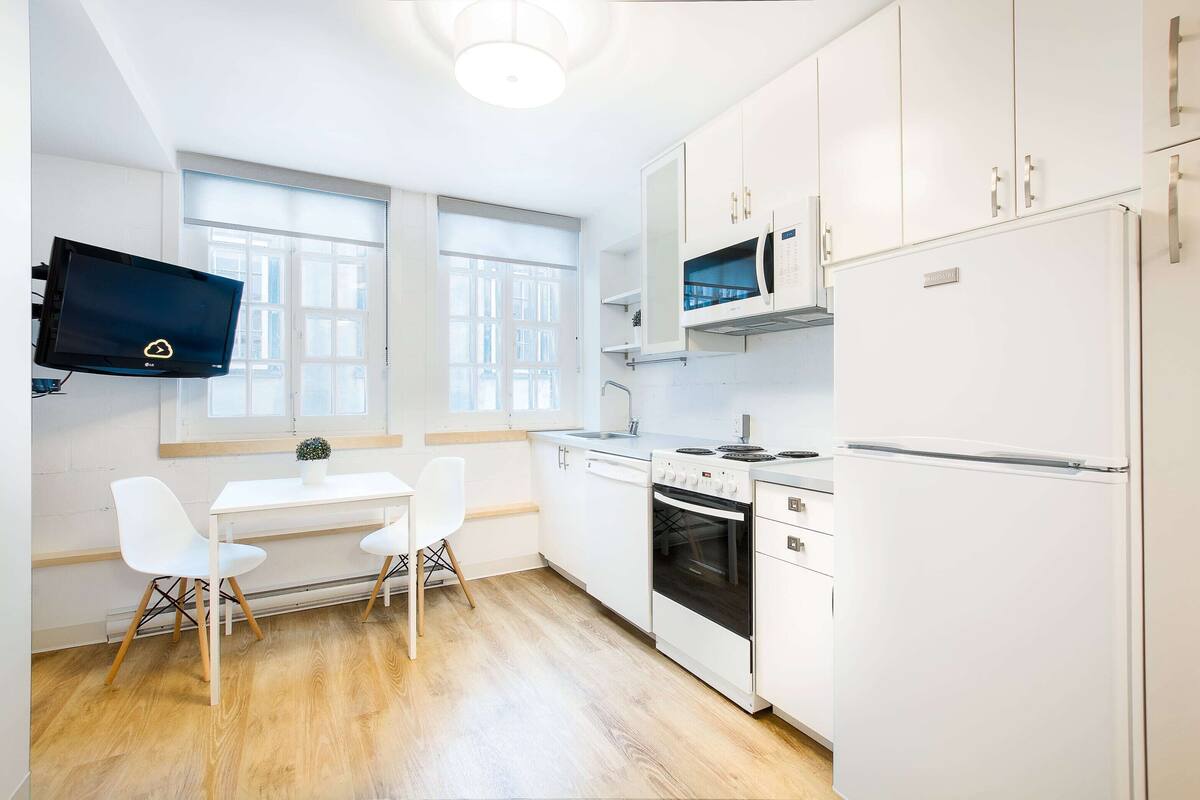 A modern kitchen with white cabinetry, a built-in oven, a microwave, and a flat-screen TV mounted above the counter.
