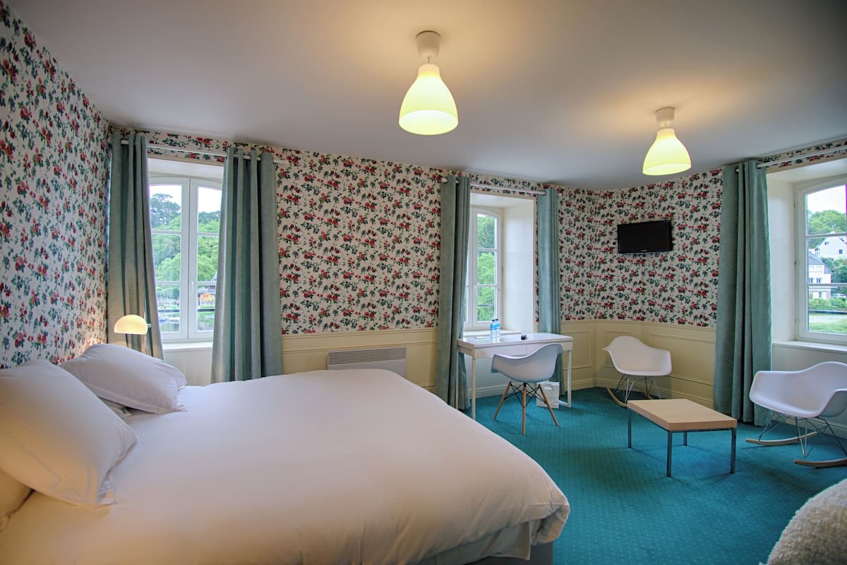 A bedroom with floral wallpaper, a bed, a desk, two chairs, and a TV on the wall.