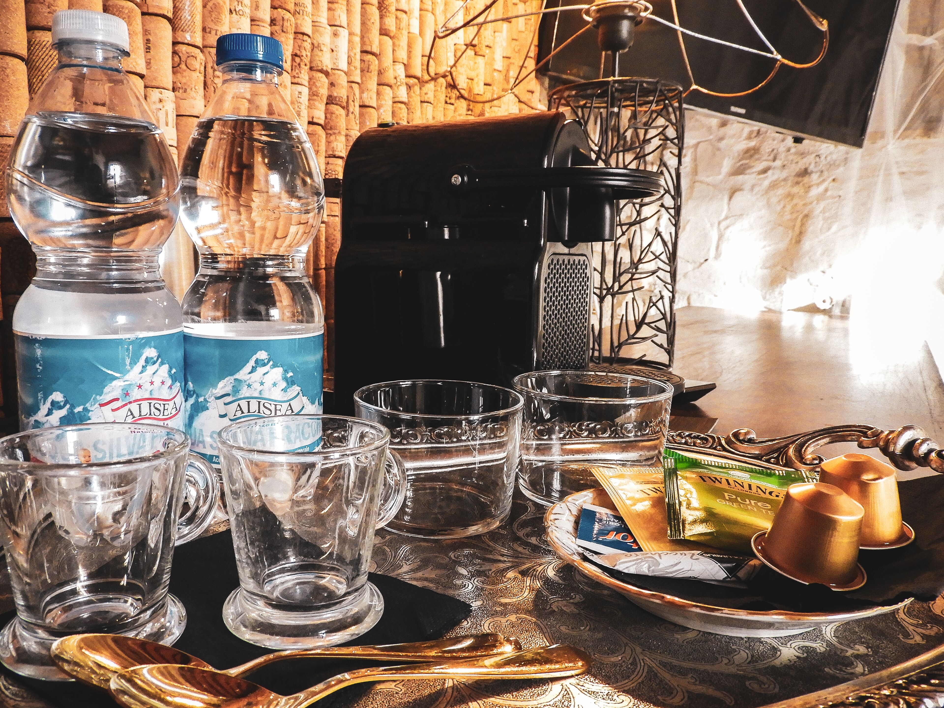 A table with water bottles, glasses, a coffee maker, and a tray with snacks.