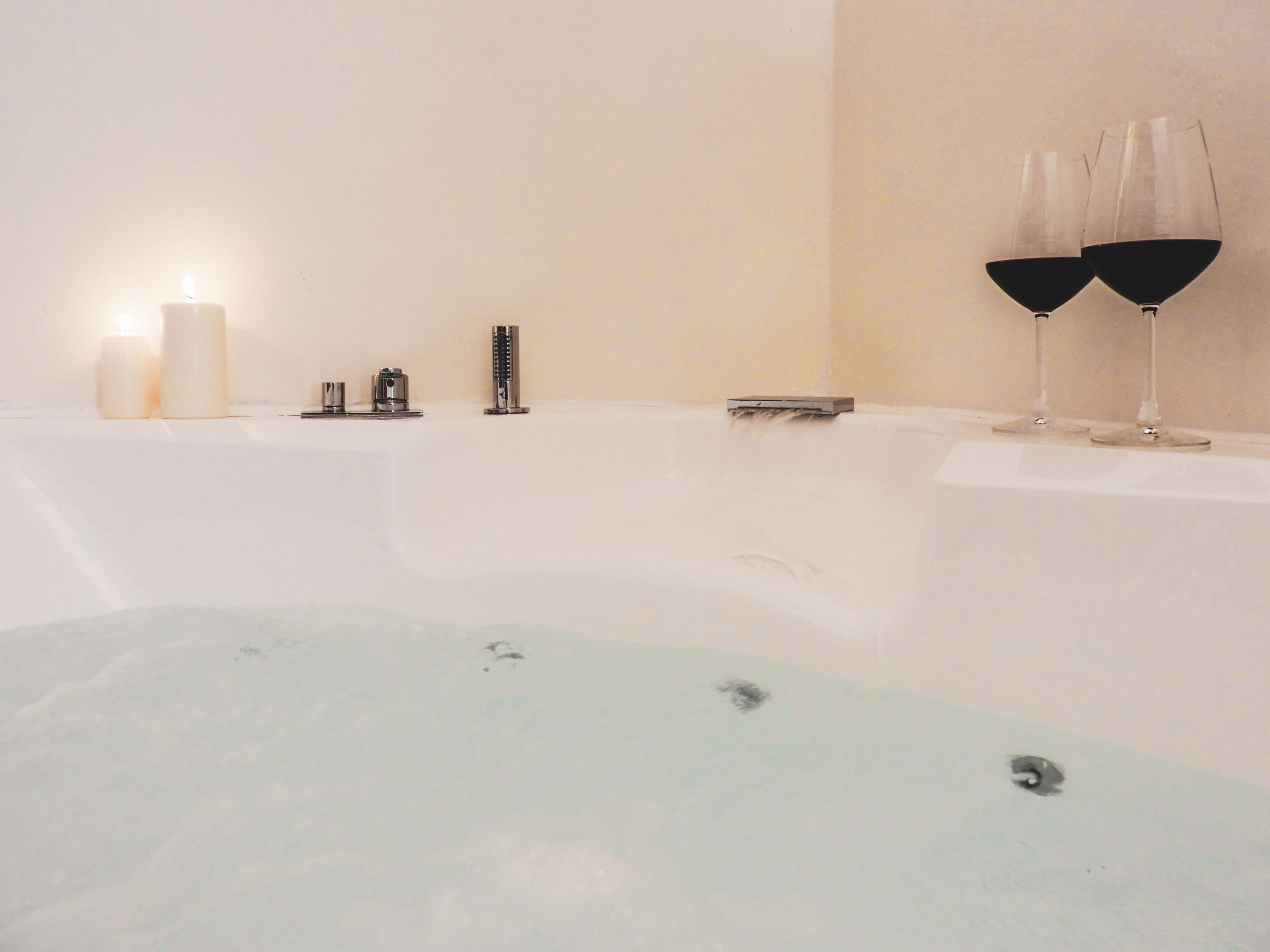 A bathtub with two glasses of red wine, a lit candle, and a small tray.