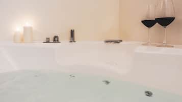 A bathtub with two glasses of red wine, a lit candle, and a small tray.