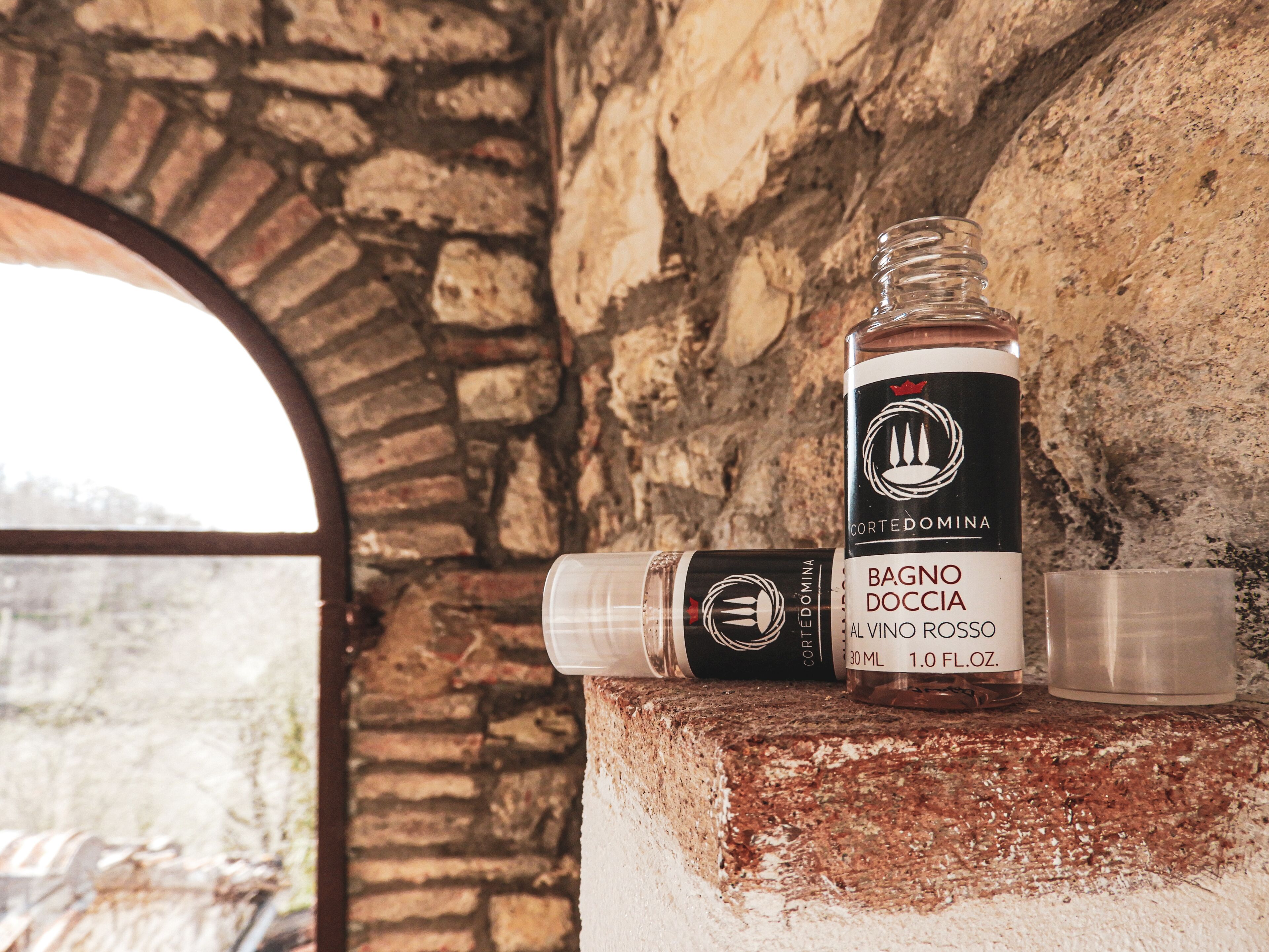 A bottle of Bagnio Doccia al Vino Rosso on a rustic stone ledge with a glass.