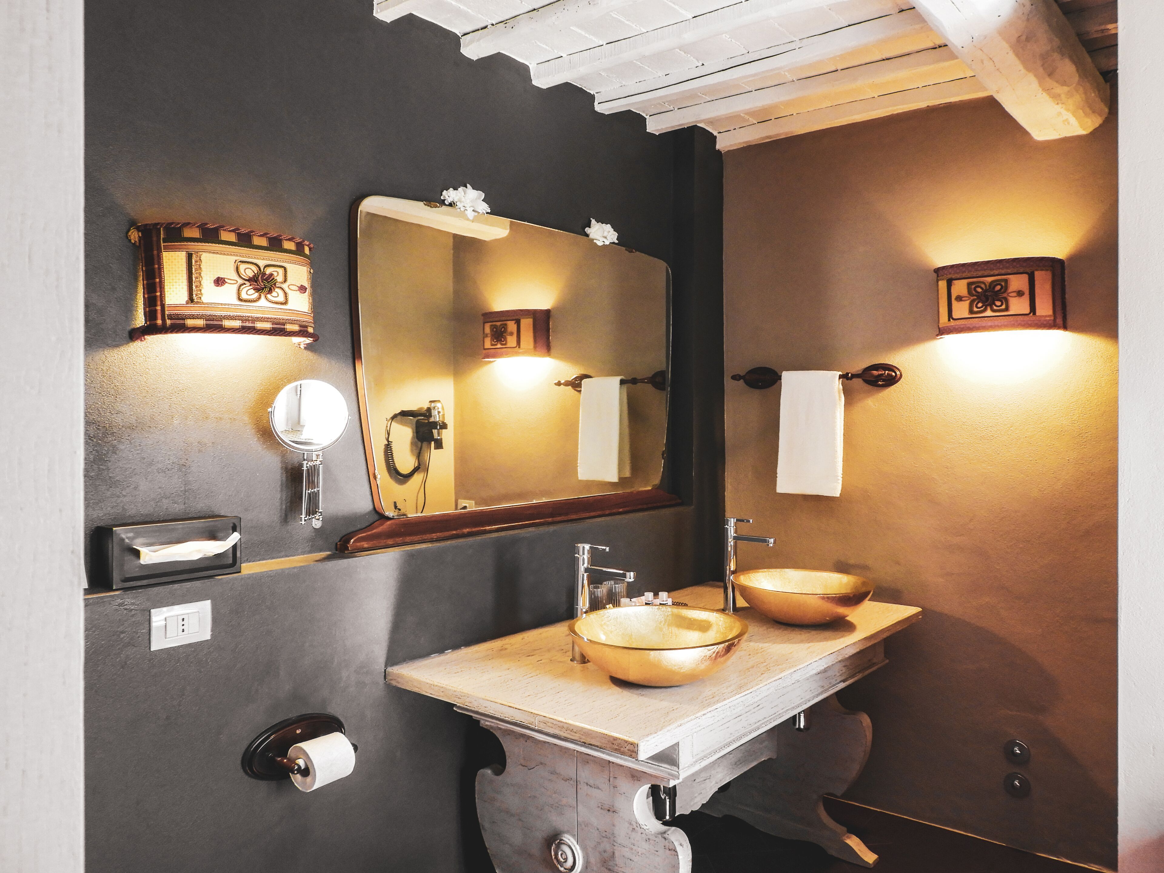 A bathroom with a large mirror, two sinks, a towel rack, and a toilet paper holder.