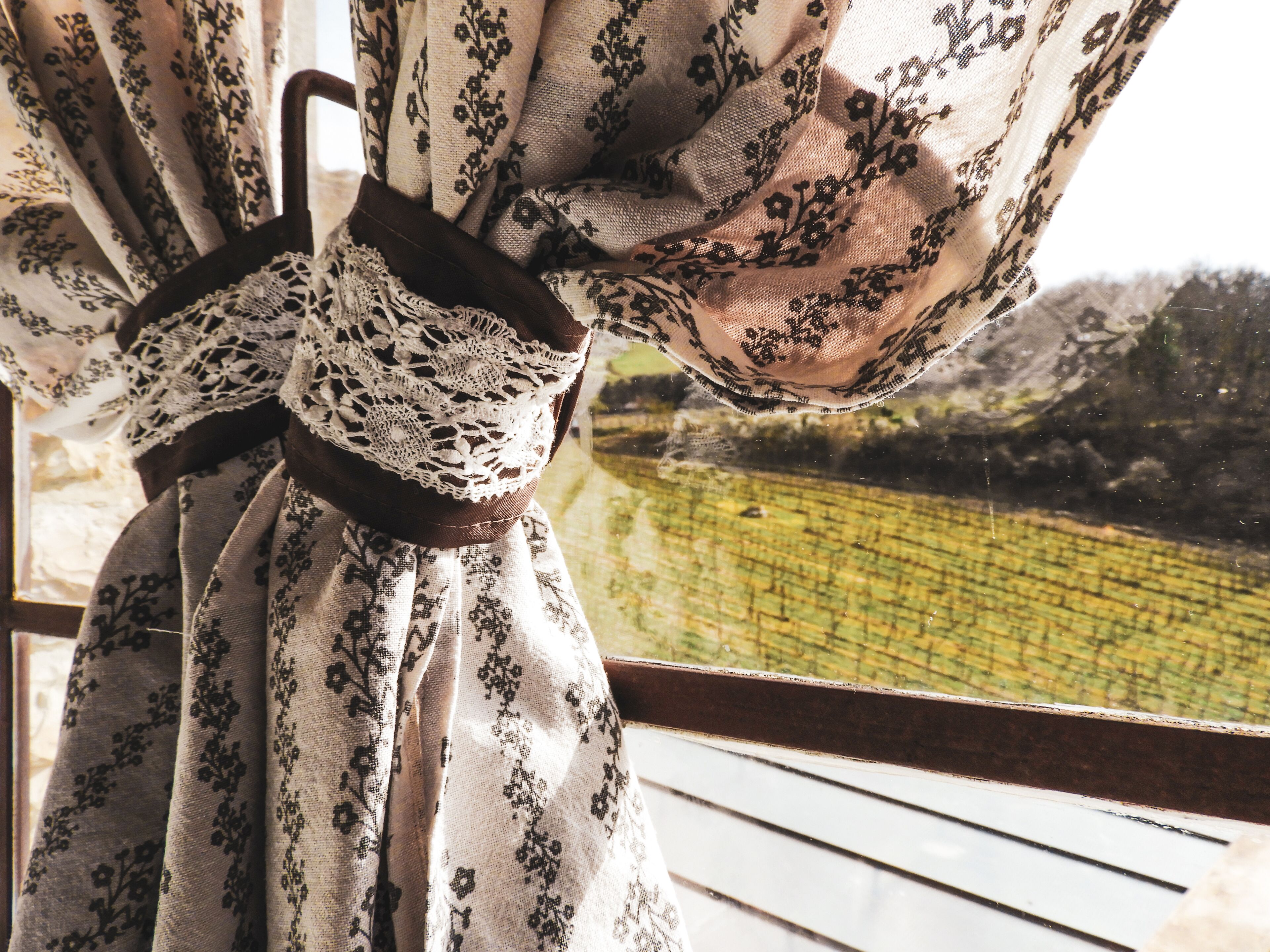 A curtain with a lace pattern and a brown ribbon tied around it.