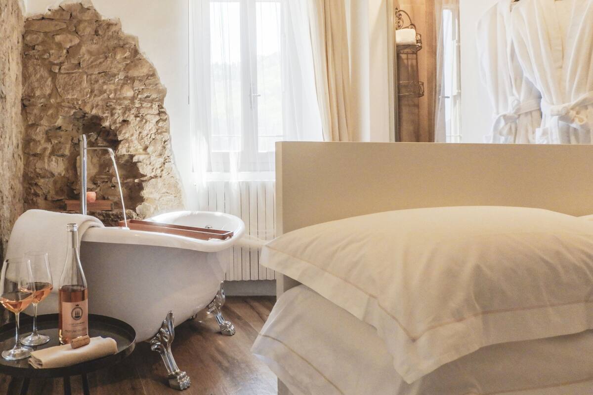 A bedroom with a stone wall, a bathtub, a bottle of wine, and a robe hanging on a rack.