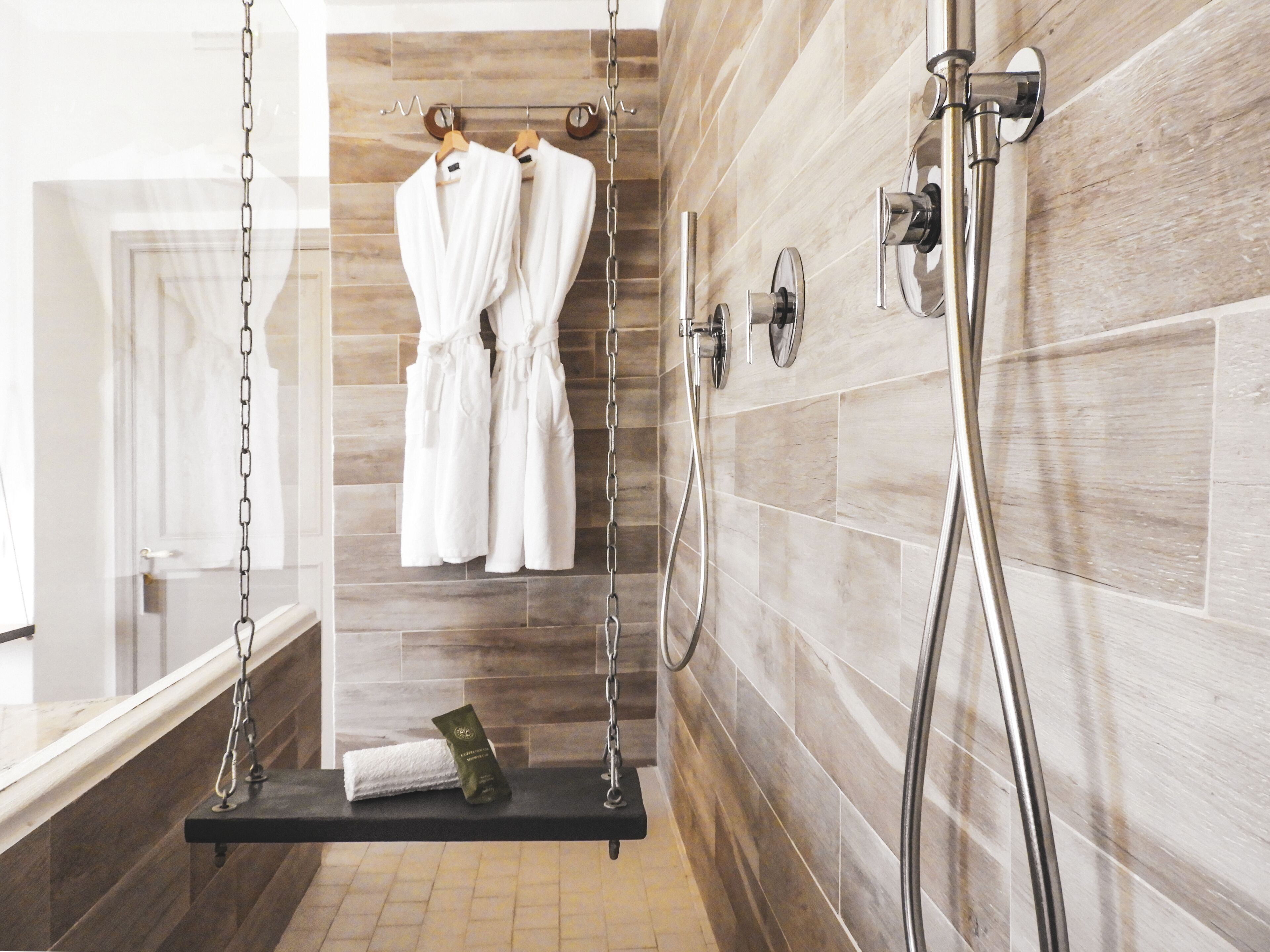 A modern bathroom with a wooden wall, a hanging robe rack, a towel rack, and a shower with a handheld showerhead.