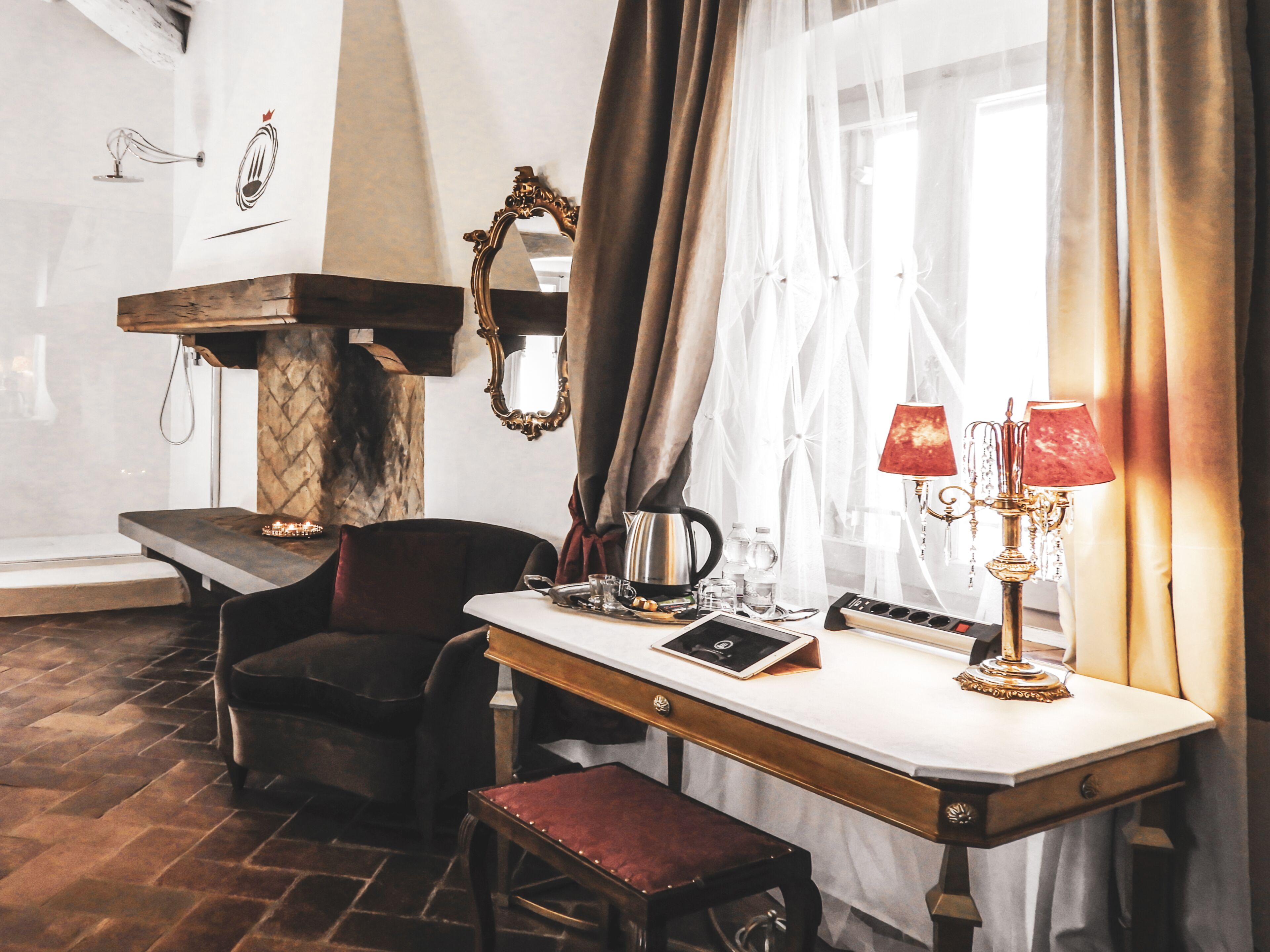 A room with a wooden bench, a table with a lamp, a chair, and a mirror on the wall.