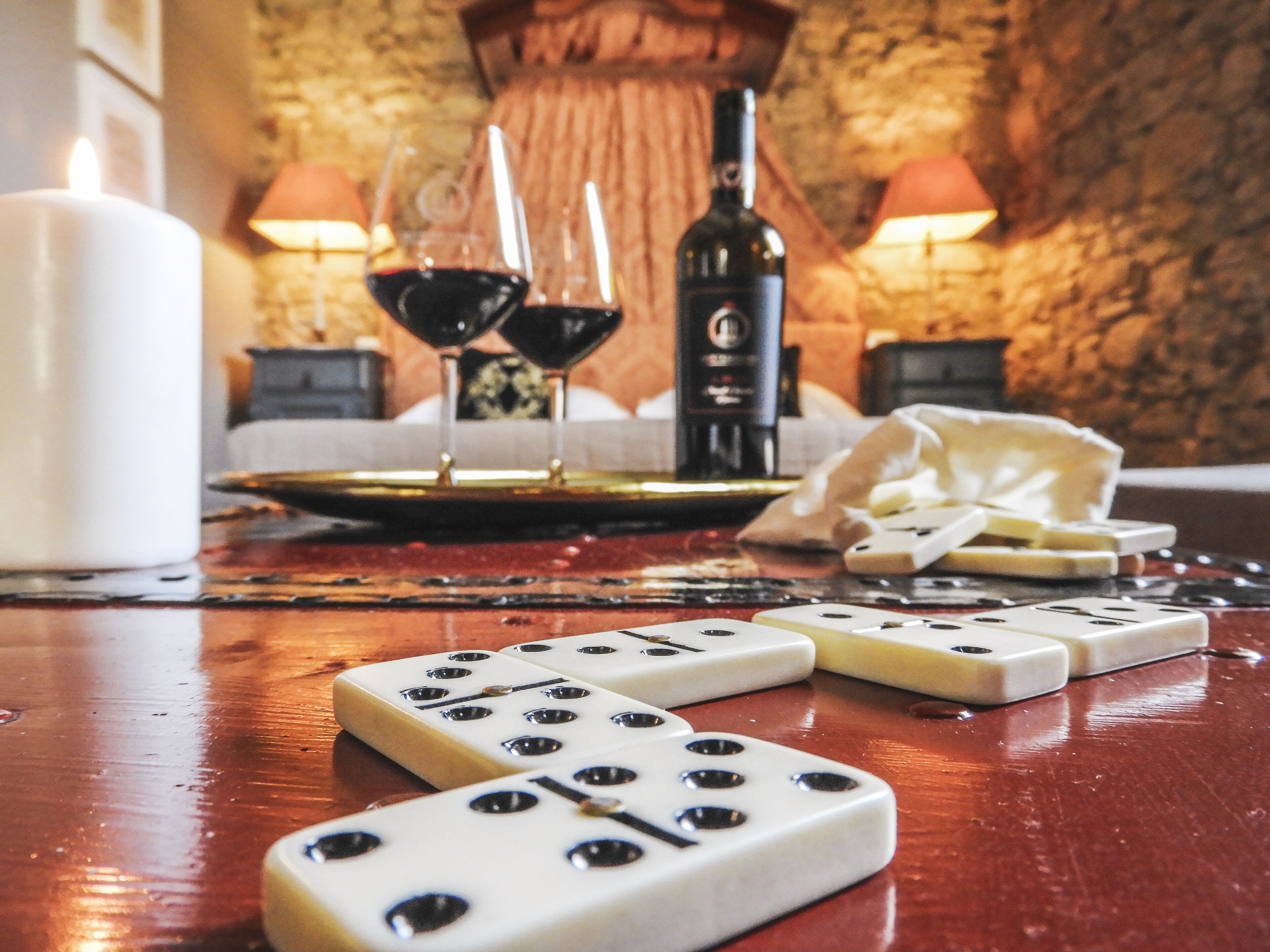A table with two dice, a candle, two glasses of red wine, a bottle, and a cheese board.