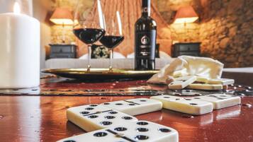 A table with two dice, a candle, two glasses of red wine, a bottle, and a cheese board.