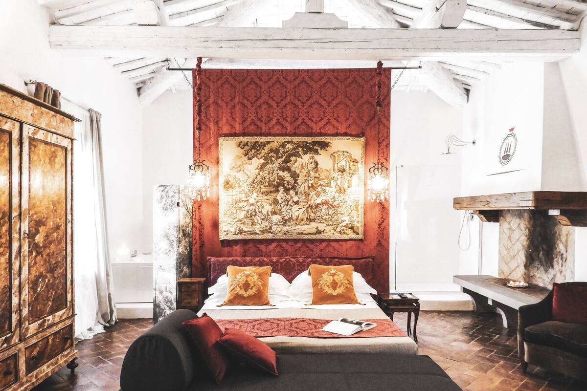 A bedroom with a large bed, a wooden headboard, a tapestry, and a chandelier.
