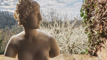 Una estatua de figura clásica domina un paisaje con árboles en flor y cielo despejado.
