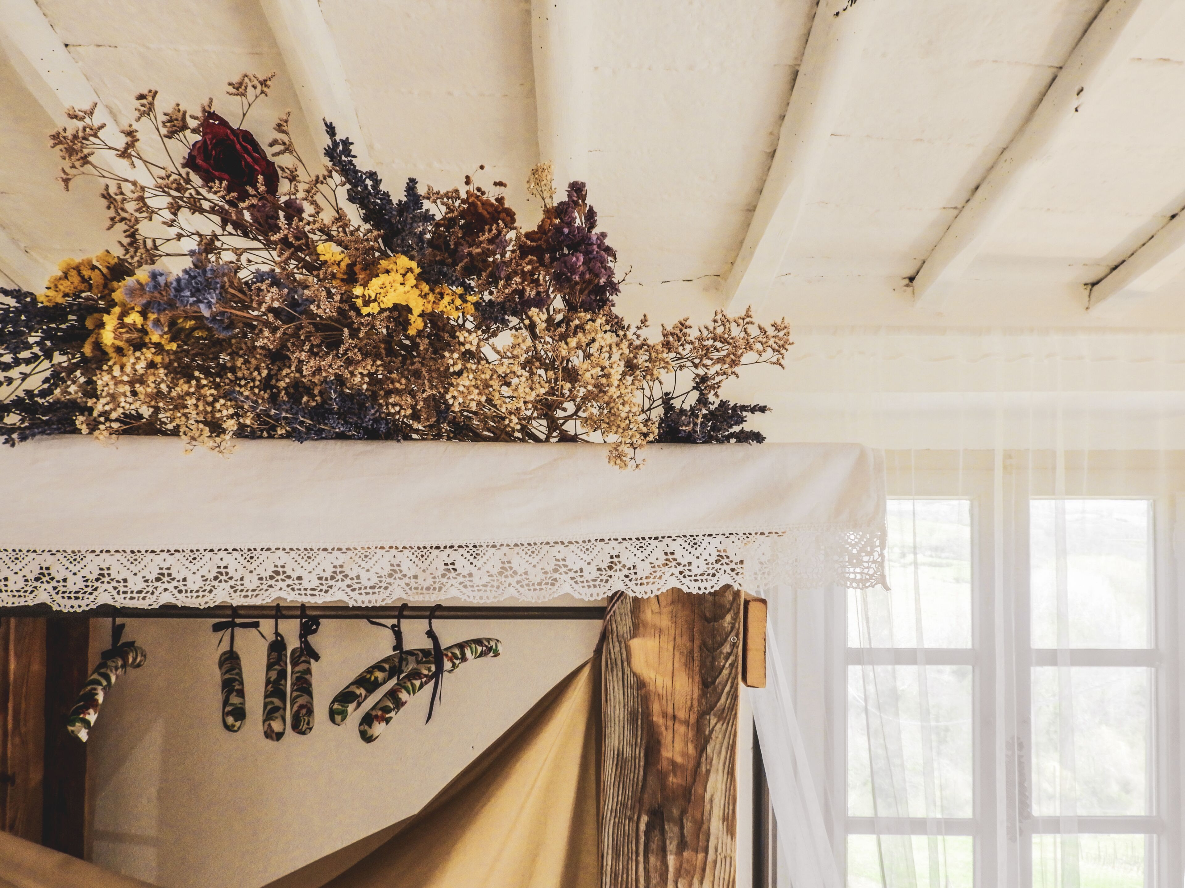 Una habitación con cama, cabecero de encaje y ventana con cortinas traslúcidas.