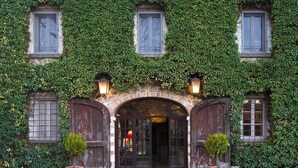 A building with a brick facade, arched entrance, and multiple windows covered in green ivy. - Tenuta CorteDomina (Radda in Chianti)