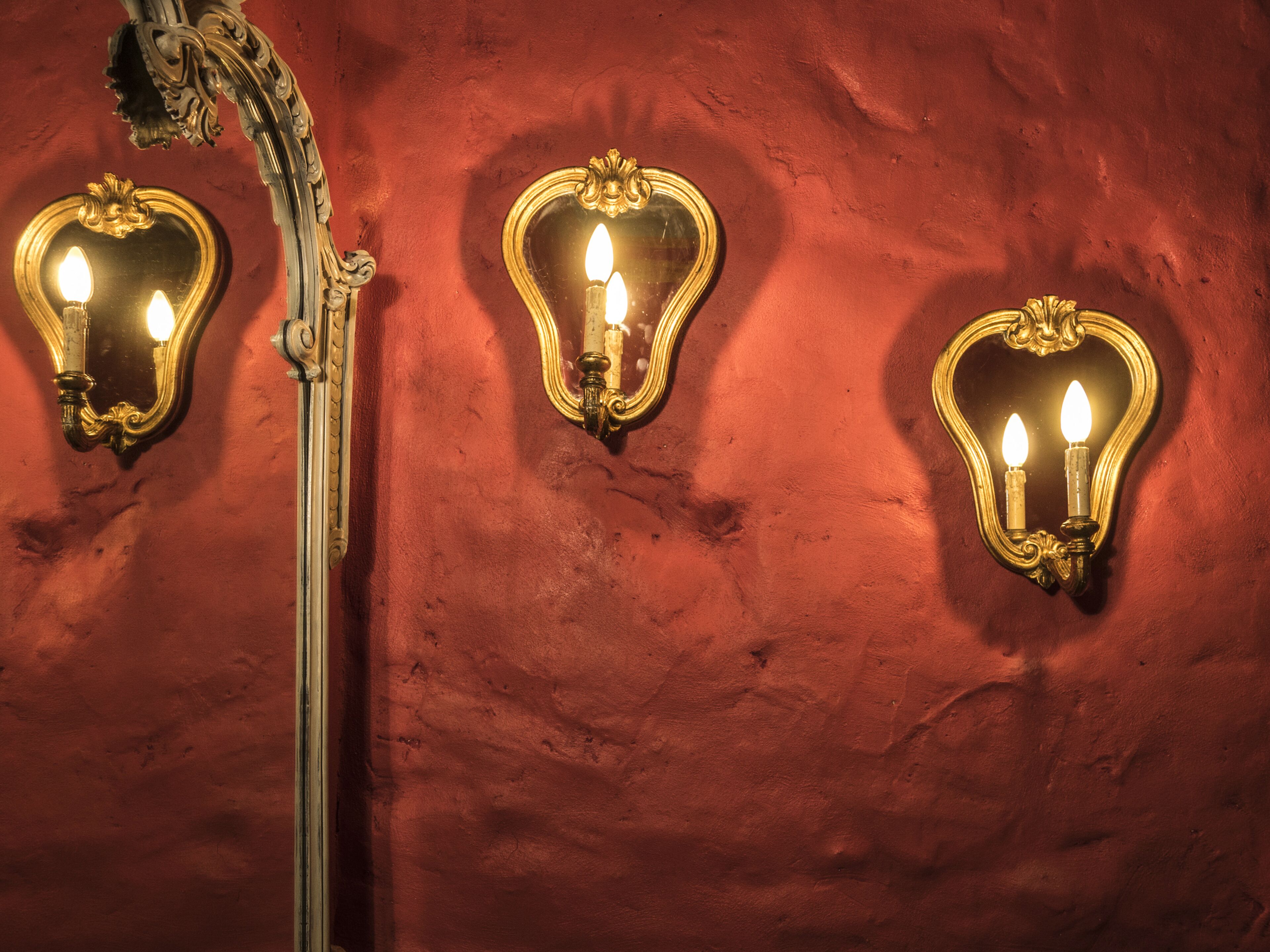 Three wall-mounted light fixtures with candle-like bulbs against a textured red wall.
