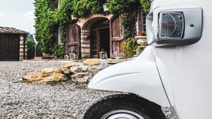 A white vehicle parked in front of a building with a stone facade and arched windows, surrounded by gravel and greenery. - Tenuta CorteDomina (Radda in Chianti)