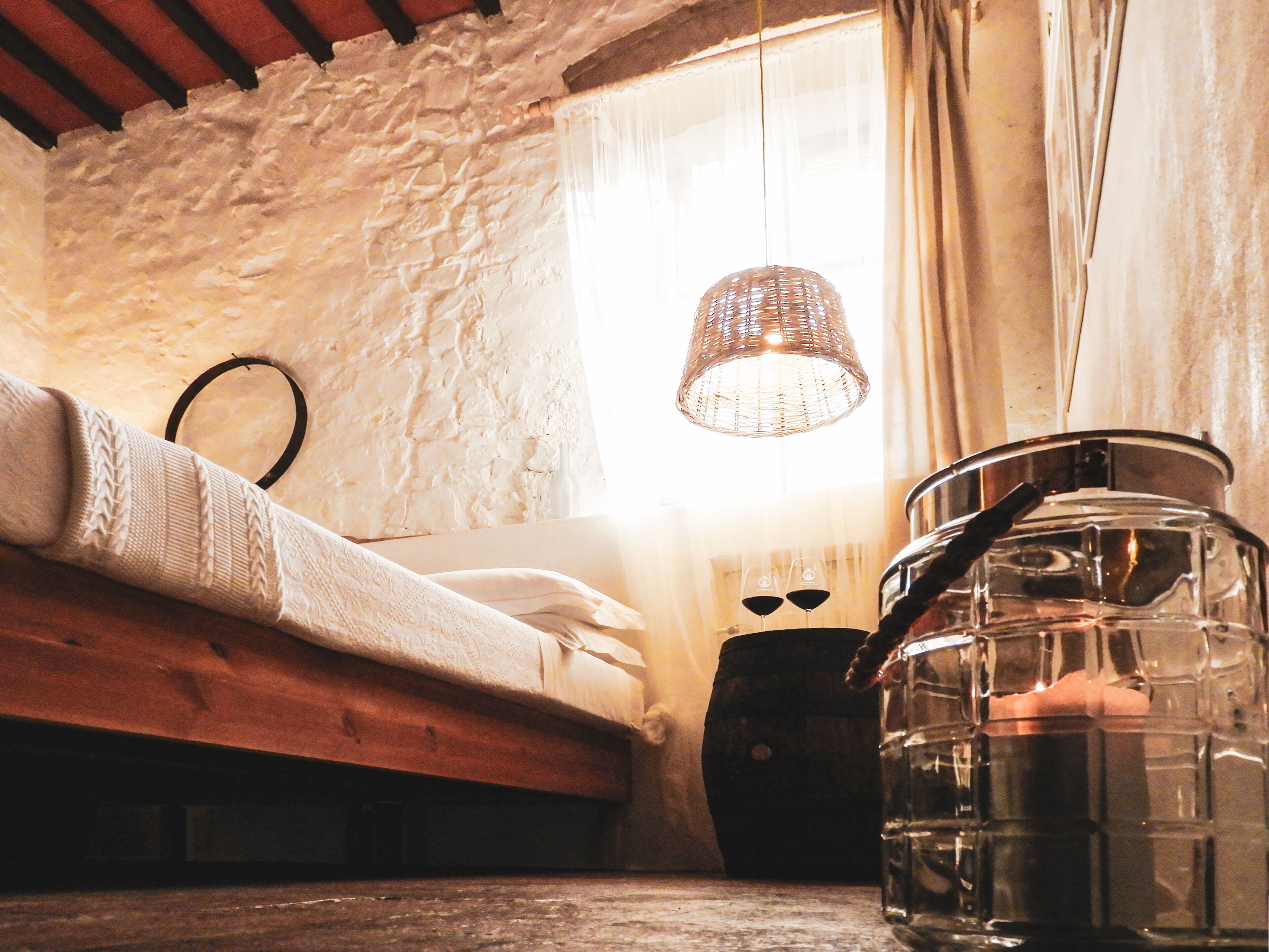 A rustic attic room with a wooden bed, a woven light fixture, and a large metal container.