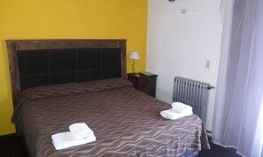 A hotel room with a bed, a nightstand, a lamp, and a radiator. - Posada Alpenrose Neu (Villa Carlos Paz)