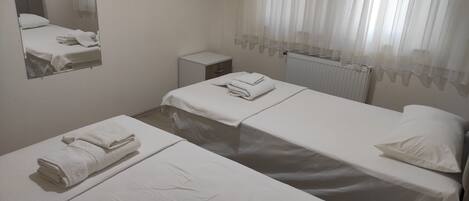 A hotel room with two beds, a small bedside table, a mirror, and a window with sheer curtains.