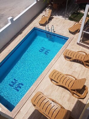 A rectangular swimming pool with clear blue water, surrounded by a tiled deck. There are lounge chairs with a curved design placed around the pool. - Villa Konak Yalcin (Ortaca)