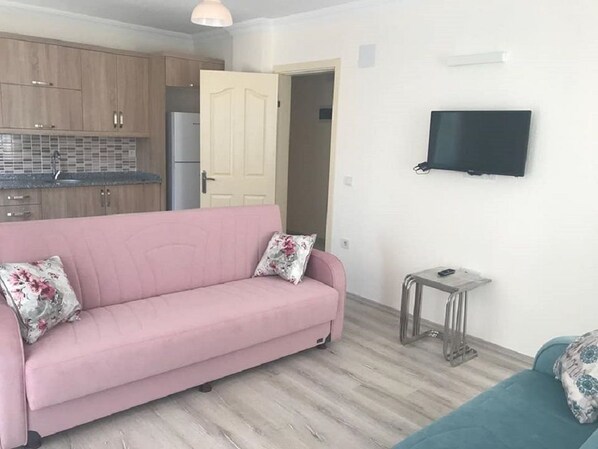 A living room with a pink sofa, a teal sofa, a small table, and a TV mounted on the wall. - Villa Konak Yalcin (Ortaca)
