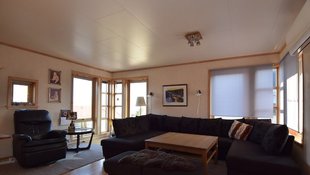 A spacious living room with a sectional sofa, a black armchair, a wooden coffee table, and a small side table. - Solferie Holiday Home Marthas vei (Kristiansand)