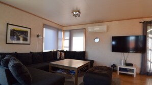 A living room with a sectional sofa, a coffee table, a flat-screen TV, and a ceiling light fixture. - Solferie Holiday Home Marthas vei (Kristiansand)