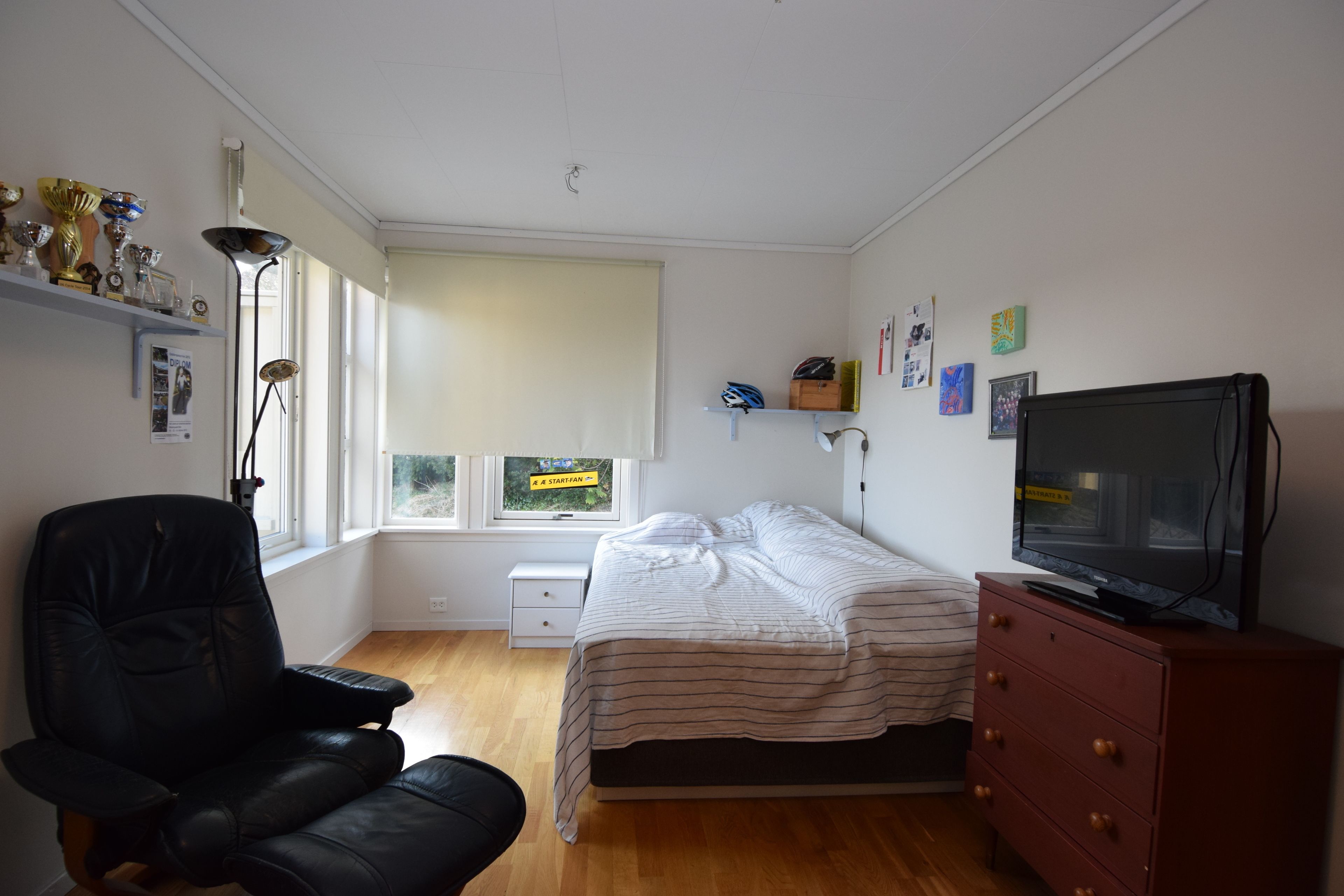 Quarto com cama, cadeira, penteadeira, televisão e janela com persianas.