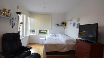 Quarto com cama, cadeira, penteadeira, televisão e janela com persianas.
