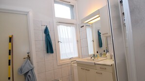 A bathroom with a bidet, a sink, a mirror, and a window with curtains. - Stay.plus King Street (Kristiansand)