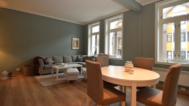 A modern living room with a grey sofa, a white coffee table, and a round dining table with chairs. - Stay.plus King Street (Kristiansand)